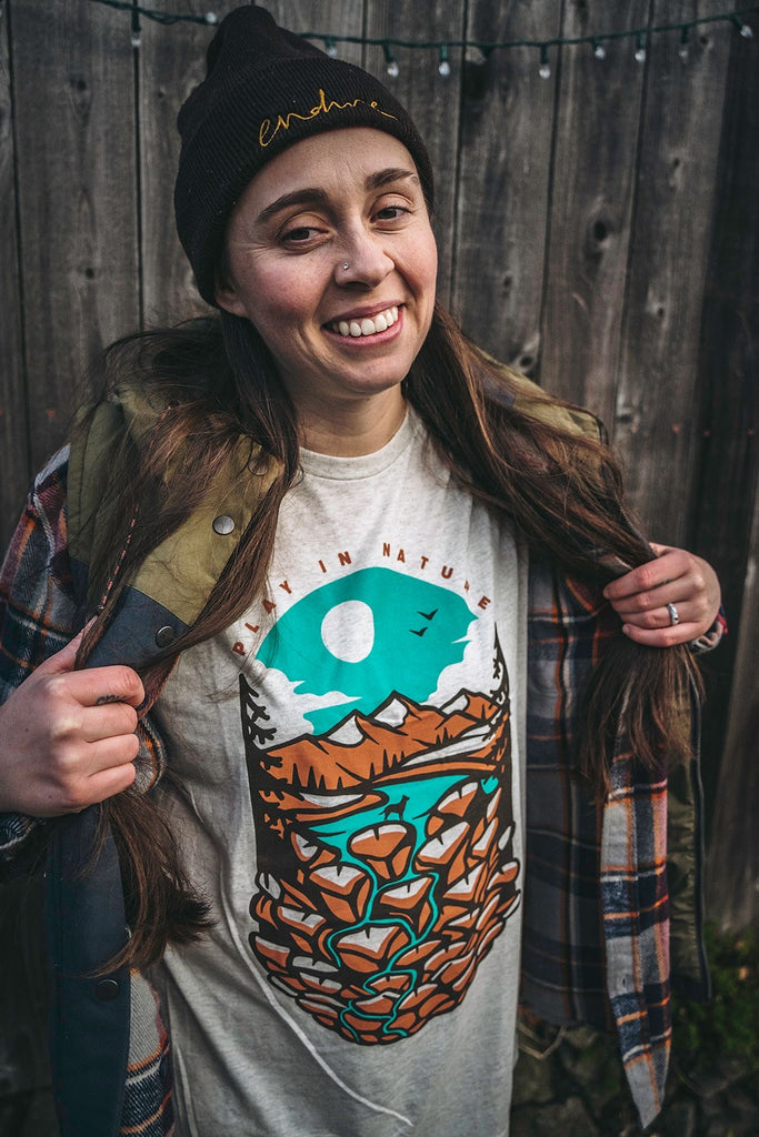 Woman smiling and wearing the Loblola Play in Nature tshirt which features a dog in a river with mountains in the background.
