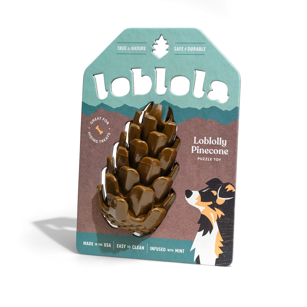 The Loblolly Pinecone Puzzle Dog Toy by Loblola in its packaging. The packaging is blue and teal and brown and shows an illustration of Lola, a black-tri australian shepherd.