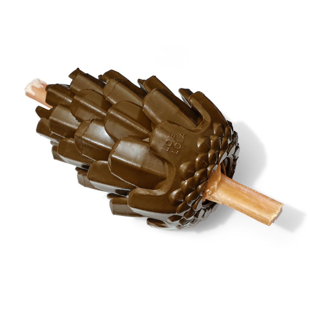 The Loblolly Pinecone Puzzle Dog Toy by Loblola. There is a bully stick stuck through the inside hollow at the bottom and coming out the top hole of the Pinecone.